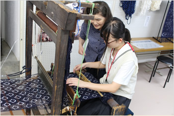 伊予かすりの普及活動をしている、伊予農業高等学校の生徒の皆さんの発表の場に。伝統工芸士の方から、織の手ほどきを受ける。